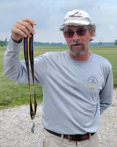 Man holding medals outdoors, wearing a cap and sunglasses.