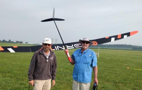 Two men with a large model glider in a grassy field.