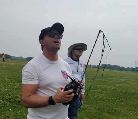 Two people in a field flying remote-controlled planes.