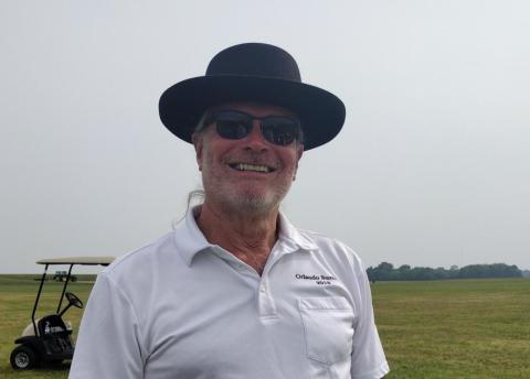 Man in a white polo and black hat smiling outdoors.