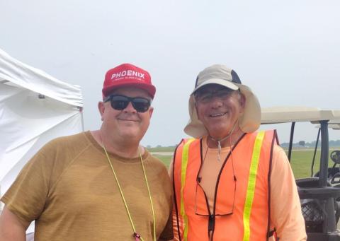 Two smiling men, one in red cap, one in safety vest, outdoors.
