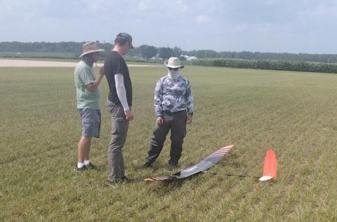 Three people examining a small glider on a grassy field.