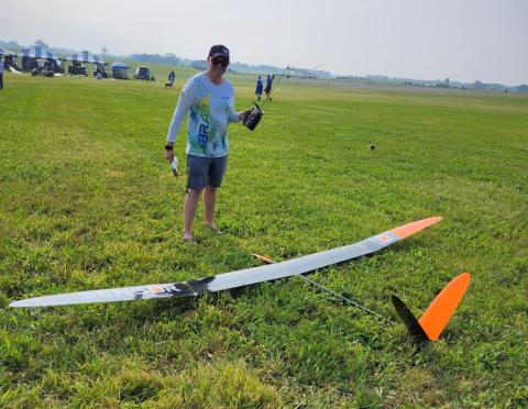 Person standing on a grassy field with a large model glider.