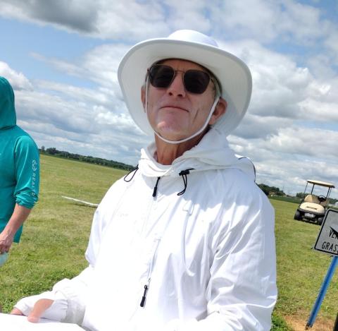 Man in white sunhat and sunglasses standing on a grassy field under a cloudy sky.