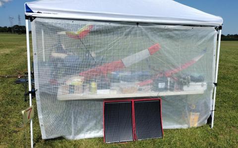 White canopy with equipment and model gliders beneath a clear tarp.