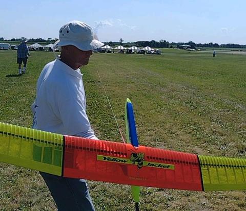 Man holding vibrant model glider in a grassy field on a sunny day.