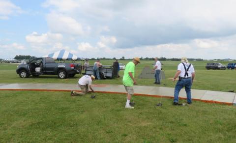 People setting up outdoor event tents on grassy field.