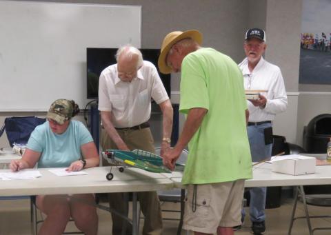 Four people examining model plane parts on a table in a casual setting.