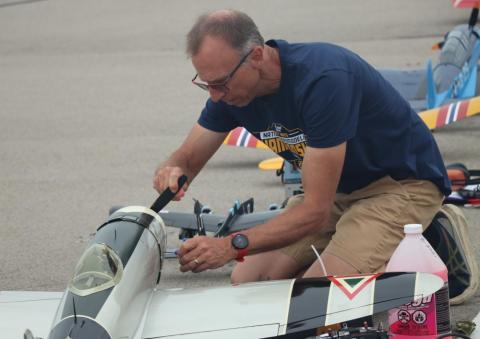 Man kneeling, adjusting a model airplane on a pavement.