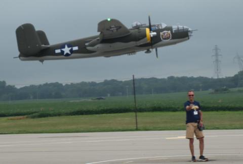 Military aircraft flying close to runway with person standing nearby.