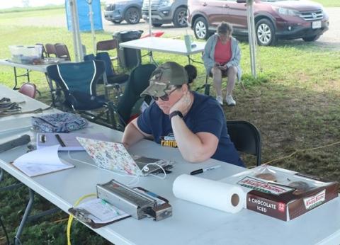 A person wearing a cap works on a laptop at an outdoor table, surrounded by supplies.