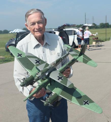 Man smiling and holding a large model military plane outdoors.
