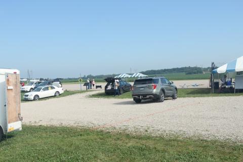 Gravel parking lot with cars and striped tents on a clear day.