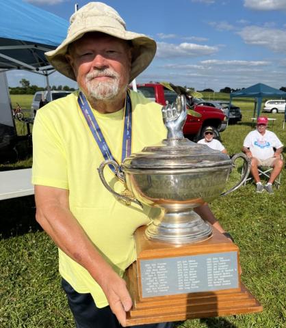 Man in yellow shirt holding a large silver trophy outdoors.