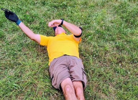 Man in yellow shirt and shorts lying on grass, covering face with one arm.