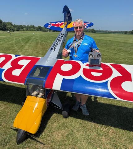 Man holding a model airplane on a grassy field, under a clear blue sky.