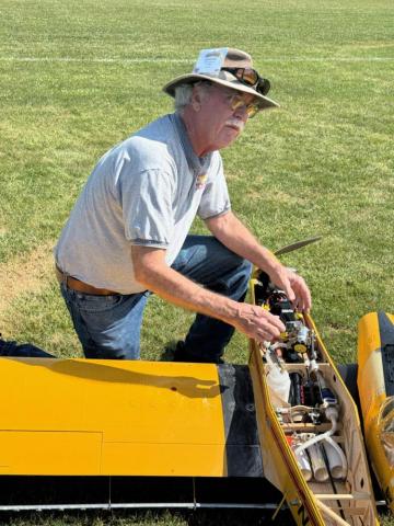 Man adjusting model plane engine outdoors on grass.