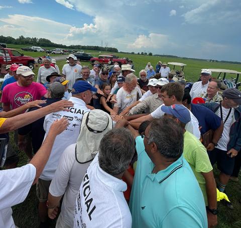 Group of people in a field, hands joined in the center.