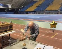 Man adjusting a small, model propeller plane on an indoor track.