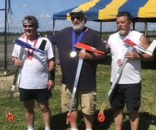 Three men with medals holding model airplanes on a sunny day.