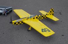 Yellow model plane with checkered black details and a propeller, on a gray surface.
