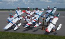 Six people with model airplanes and trophy on an airfield.
