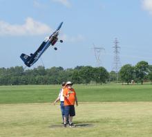 Remote-controlled plane flies low over a grassy field with power lines in the background.