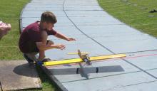 Boy kneeling, preparing a yellow model airplane on a raised track.