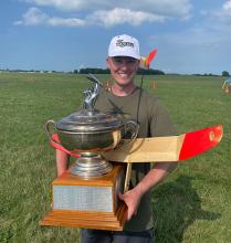 Man holding large trophy and model plane on grassy field.