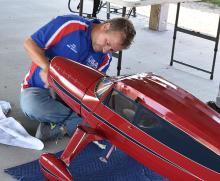 Man inspecting a red model airplane under a shelter.