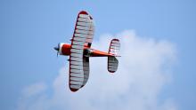 Red biplane flying against a blue sky with white clouds.
