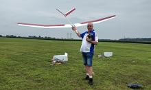 Man in a field holding a large model glider, remote control in hand.