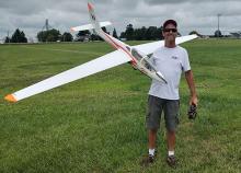 Man holding a large model airplane on a grassy field.