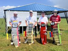 Four people holding model planes and awards, standing on grass near a pavilion.