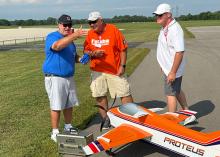 Three men laughing near a model airplane on a runway.