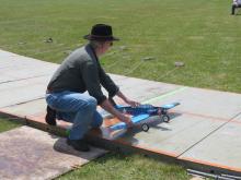 Man kneeling, launches small blue model airplane on grassy field.