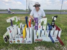 Man in sunhat smiling beside model planes on grass.