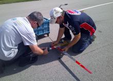 Two men adjusting a red model airplane on a paved surface.