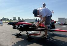 Man inspecting a model airplane on a sunny tarmac; another man stands nearby.
