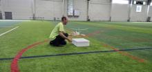 Man kneeling on indoor field with drone and box.