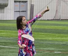 Young girl aiming a wooden bow and arrow indoors on a grass field.