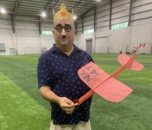 Man in crown holds a red model plane in an indoor sports facility.