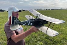 Man holding a green model biplane in a grassy field.