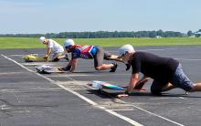 Four people on knees racing small model airplanes on a paved track.
