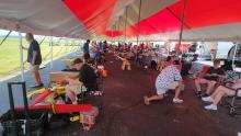 Tent with people setting up model airplanes on a sunny day.
