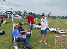 Four men beside model planes at an outdoor event.