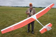 Man happily holding a large, orange remote-controlled glider on a grassy field.