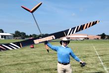 A person holding a large remote-controlled glider smiling in an open grassy field.