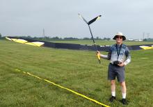 Person smiling, holding a large model glider on grassy field.