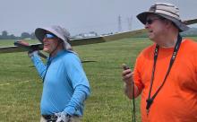 Two men in hats standing on a field with a model airplane.